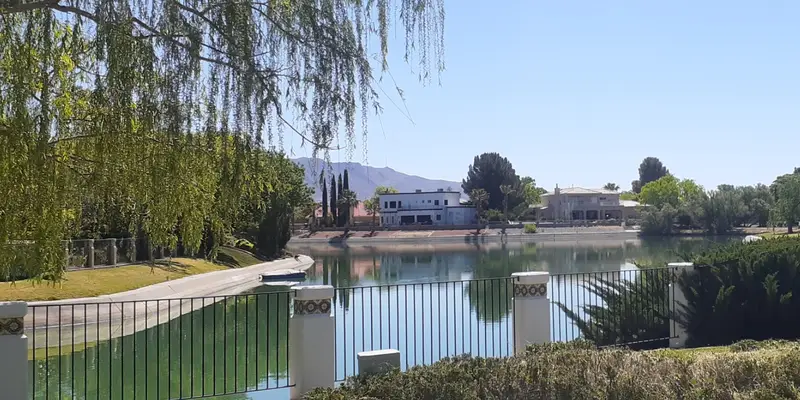 Homes and mature trees around a lake in the Upper Valley of El Paso, with the Franklin Mountains behind.